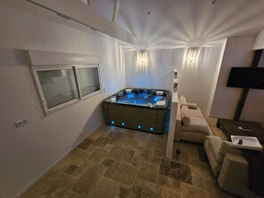 Ein Wellnessbereich mit Whirlpool, einer Couch und einem Fernseher.