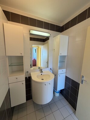 Une salle de bain avec un lavabo blanc, un miroir et des armoires, et un carrelage noir et blanc.