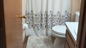 A bathroom with a shower curtain, toilet, and a white rug.