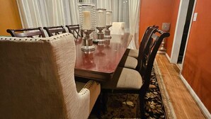 A dining room with a wooden table, chairs, a chandelier, and a patterned rug.