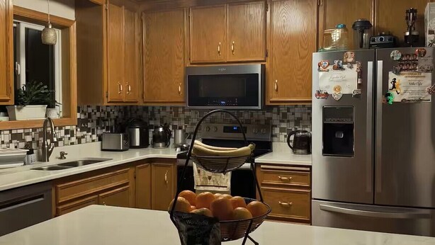 A kitchen with wooden cabinets, a microwave, a refrigerator, and a fruit basket on the counter.