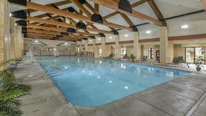 Una piscina interior con agua cristalina azul, rodeada de tumbonas y plantas en macetas.