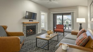A living room with a fireplace, a television, a sofa, a coffee table, and a balcony with a view.