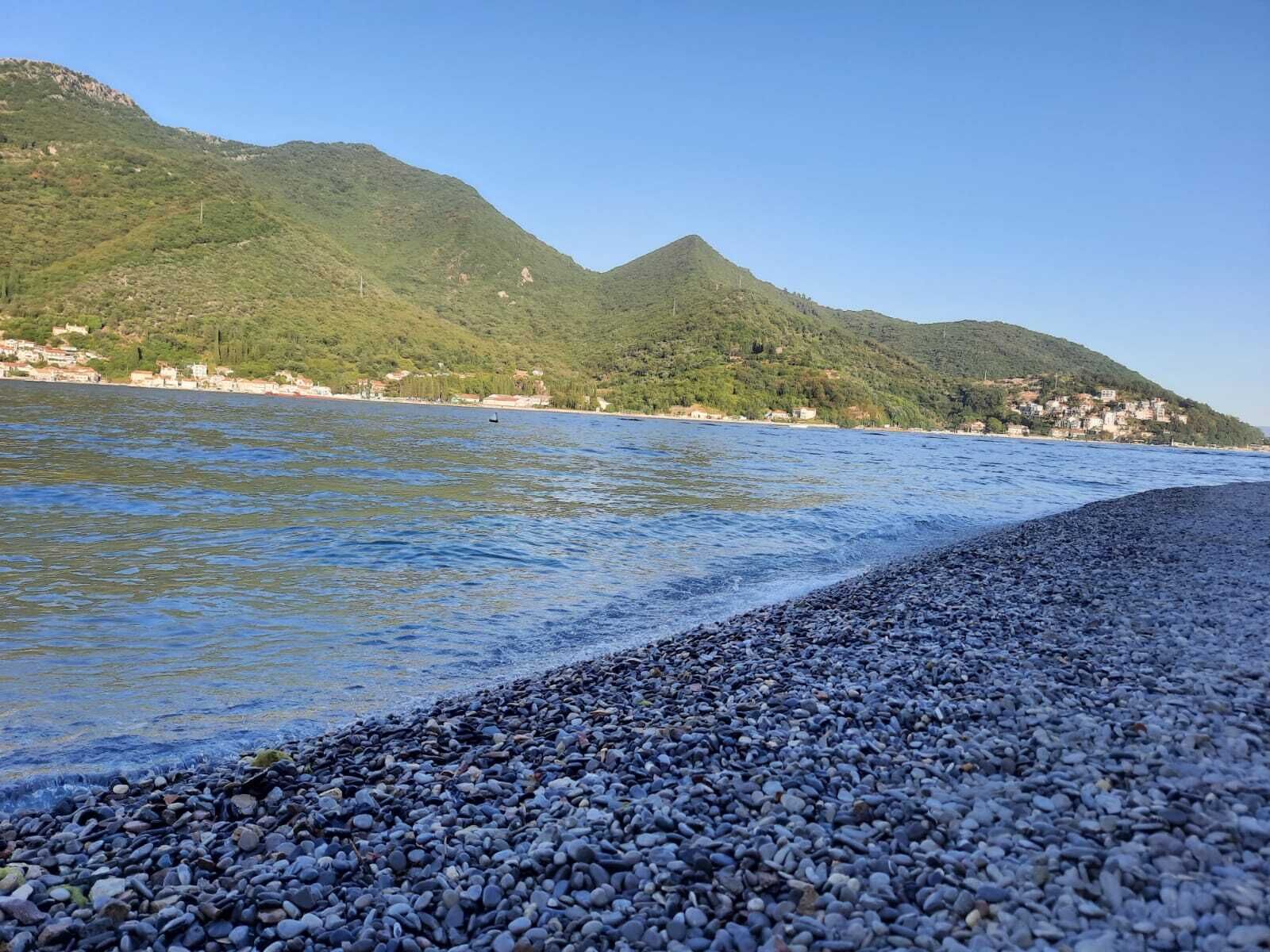 Une plage de galets avec une chaîne de montagnes en arrière-plan et un ciel dégagé.