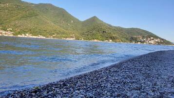 Une plage de galets avec une chaîne de montagnes en arrière-plan et un ciel dégagé.