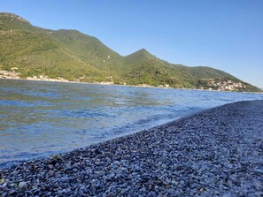 Una playa de guijarros con una montaña al fondo y cielo despejado.