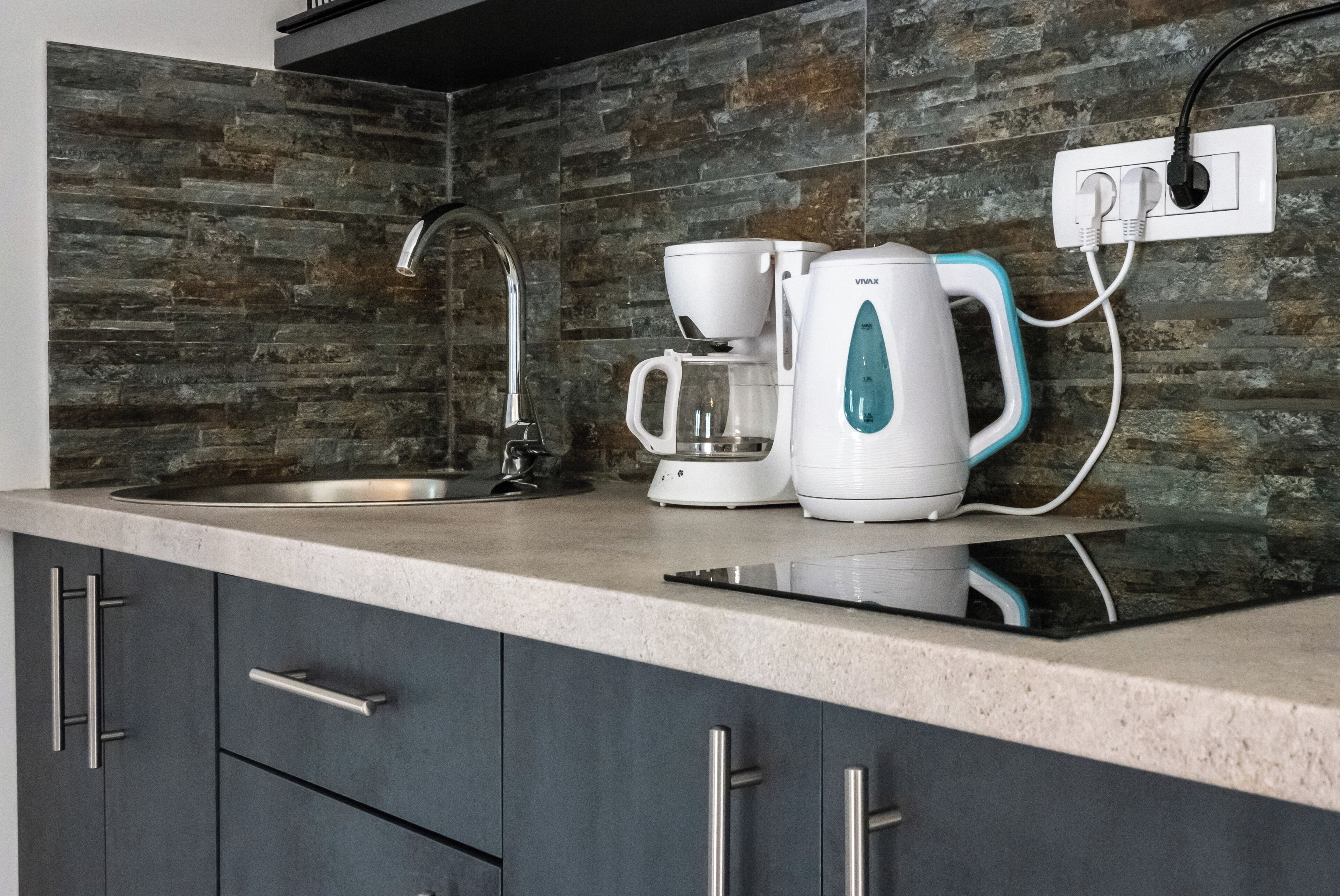 A modern kitchen with a stone backsplash, a coffee maker, and a kettle on the counter.