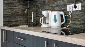 A modern kitchen with a stone backsplash, a coffee maker, and a kettle on the counter.