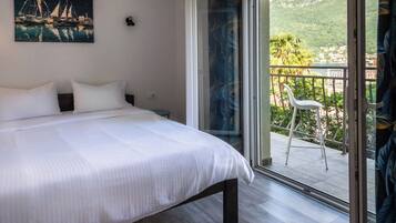 Ein Schlafzimmer mit einem Bett, einem Nachttisch, einem Gemälde und einer Schiebetür, die auf einen Balkon mit einem Stuhl führt.