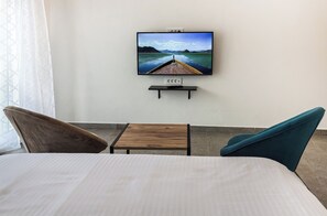 Een hotelkamer met een bed, een klein houten tafeltje, twee stoelen, een aan de muur bevestigde televisie en uitzicht op water.