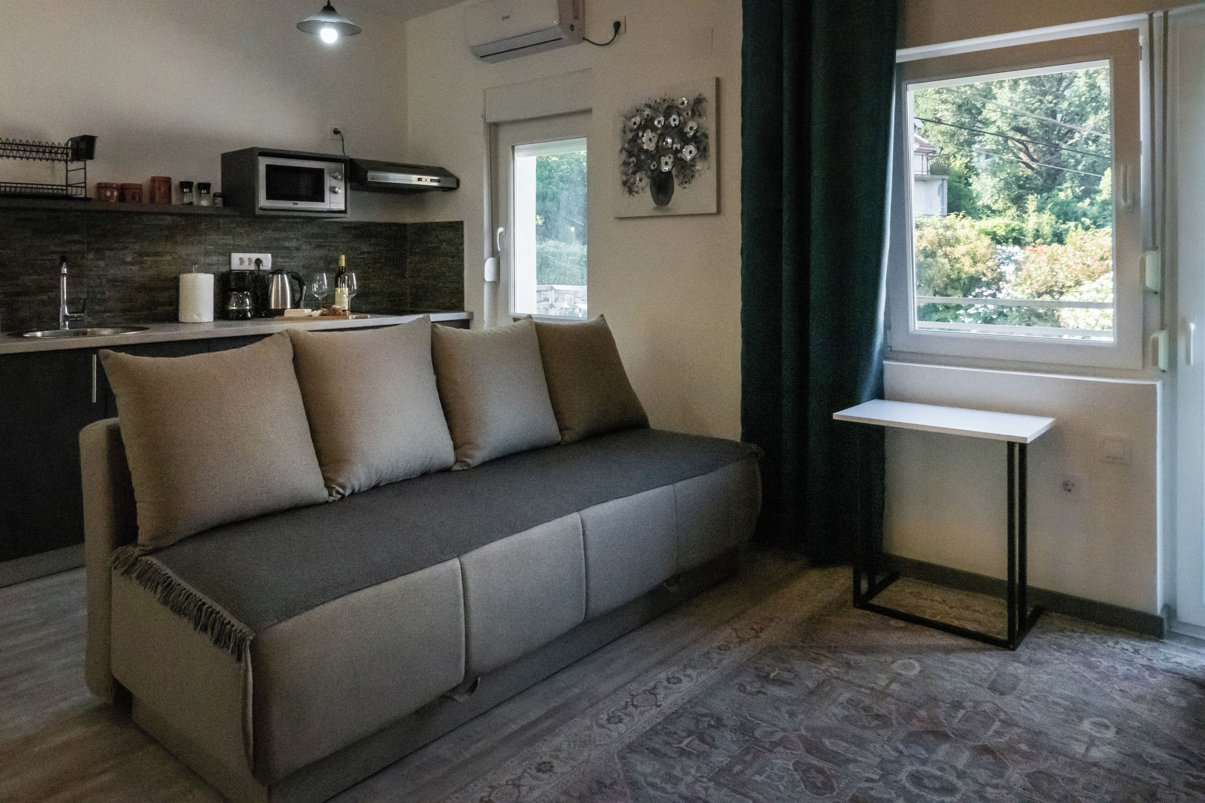 Un salon moderne comprenant un canapé, une petite table, un coin cuisine avec un four à micro-ondes et une fenêtre donnant sur un espace verdoyant.