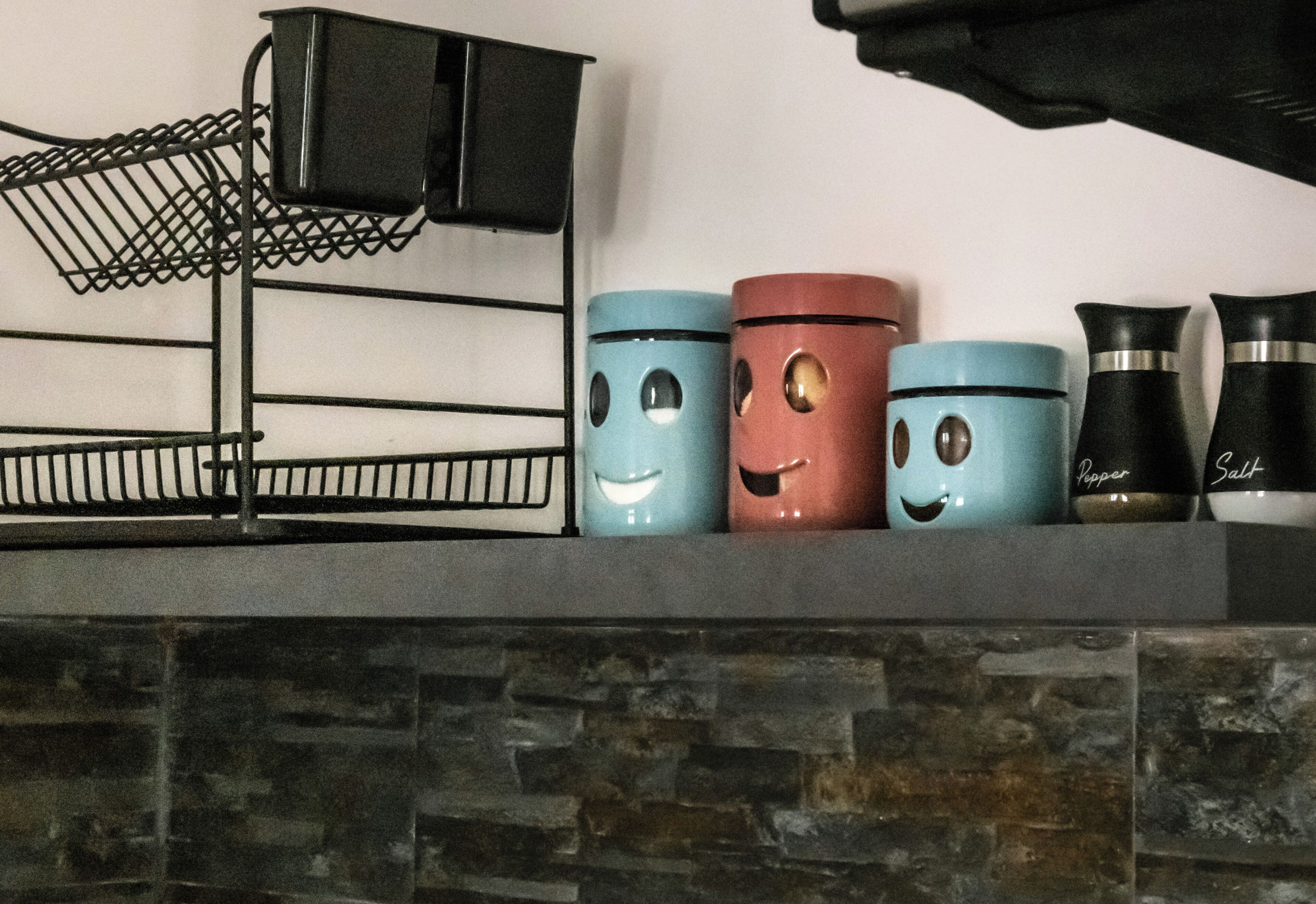 A kitchen shelf with a black wire rack and three spice containers with faces.