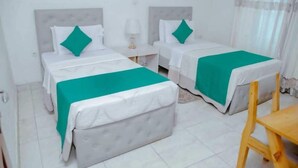 A hotel room with two beds, a small table, and a chair. - Martin aviator hotel (Kigali)