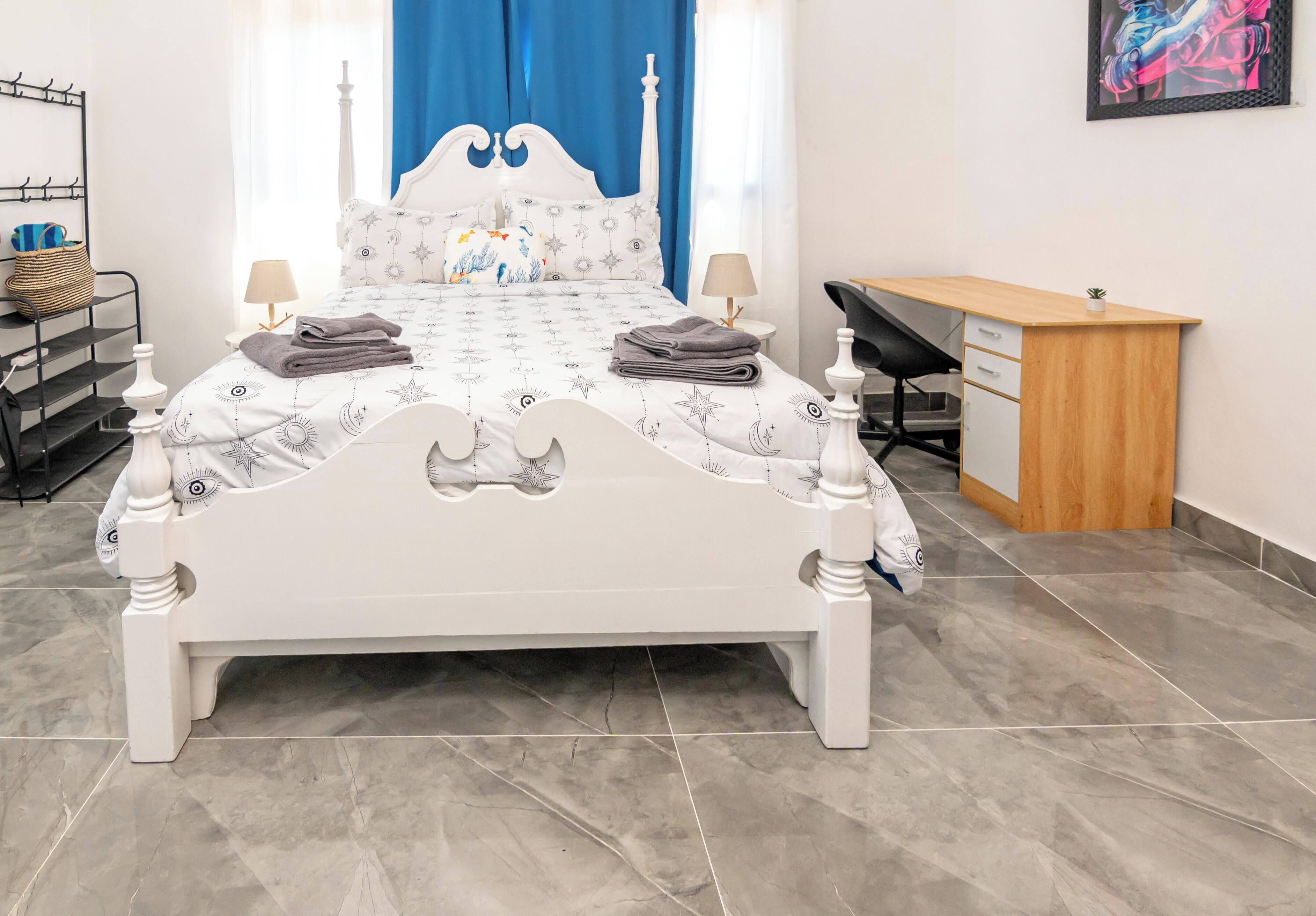 A neatly arranged bedroom with a bed, bedside tables, a desk, and a chair.