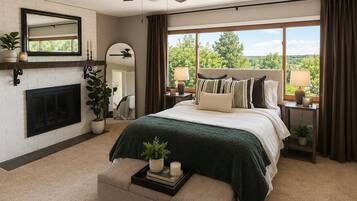 A bedroom with a large bed, a fireplace, a ceiling fan, and a view of the outdoors.