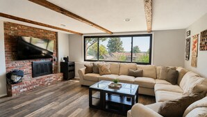 Ein Wohnzimmer mit Kamin aus Ziegelsteinen, einer Couch, einem Couchtisch und einem großen Fenster.