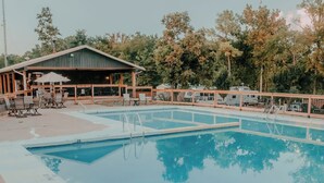 Ein Schwimmbad mit Holzterrasse, Liegestühlen und einem überdachten Pavillon.