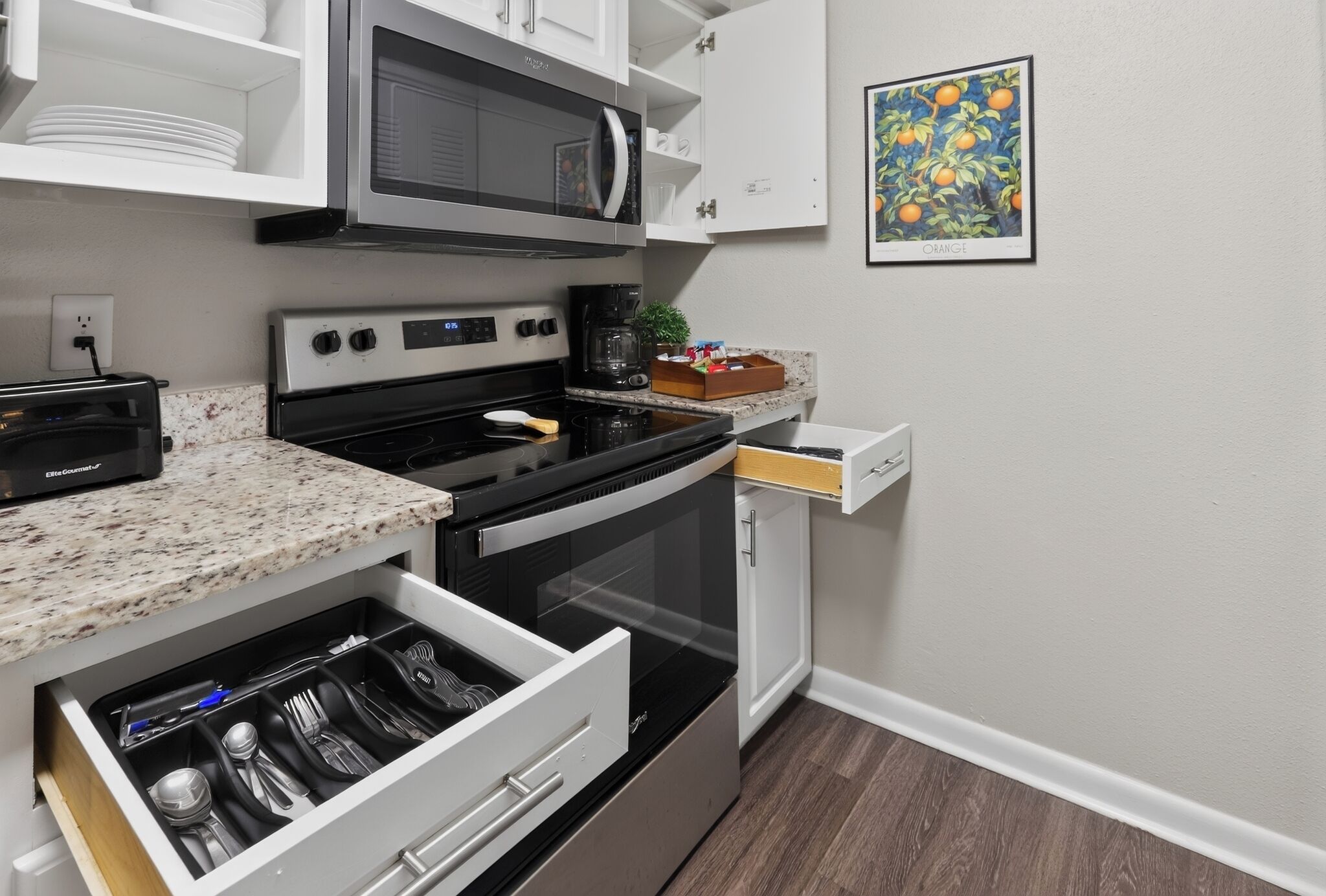 A kitchen with a microwave, stove, and oven, a drawer with utensils, and a framed picture on the wall.