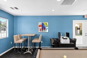 Quarto com parede azul, uma mesa com cadeiras, uma impressora e um sinal de saída.