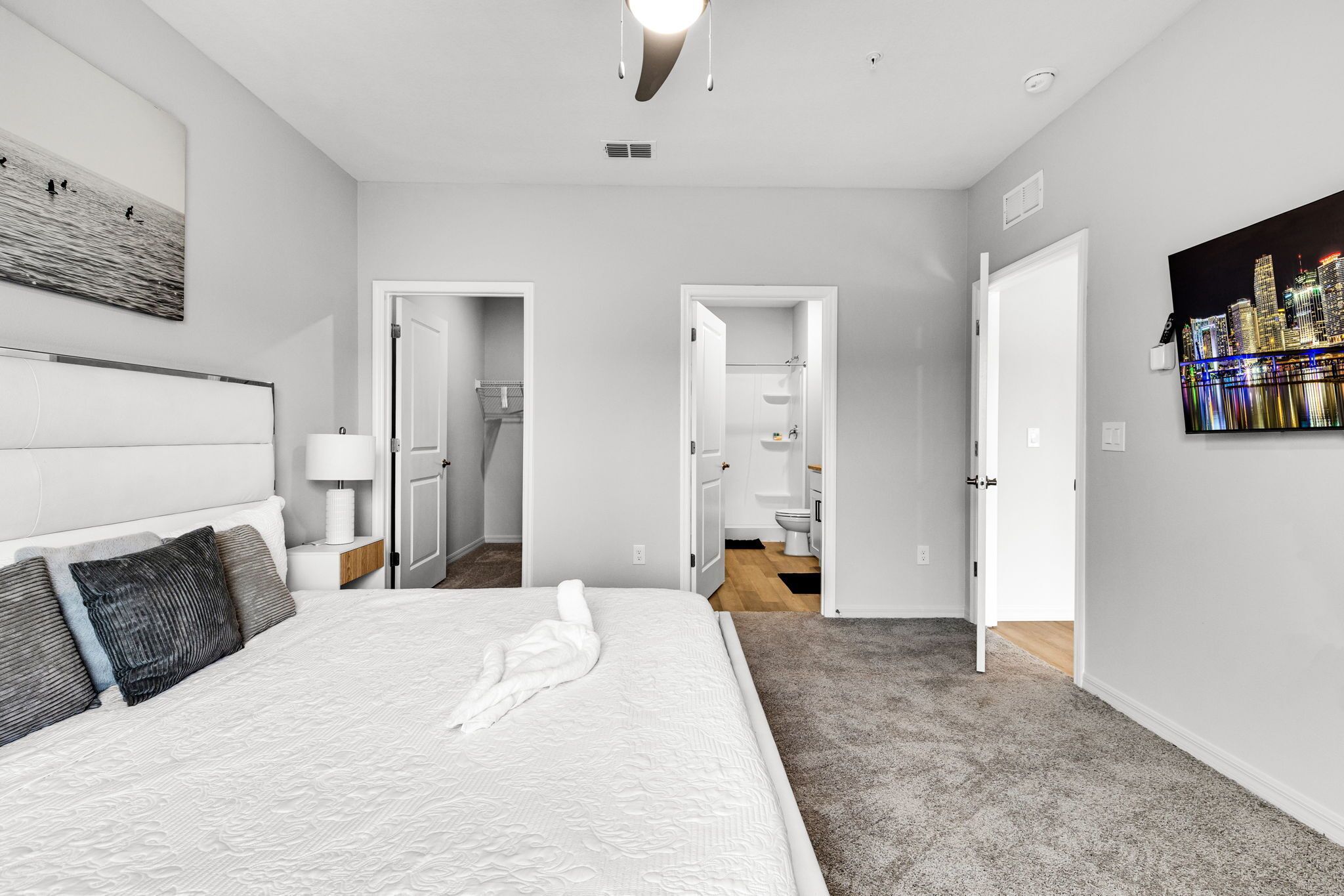 A modern hotel room with a large bed, a nightstand, a wall-mounted lamp, and a cityscape painting.