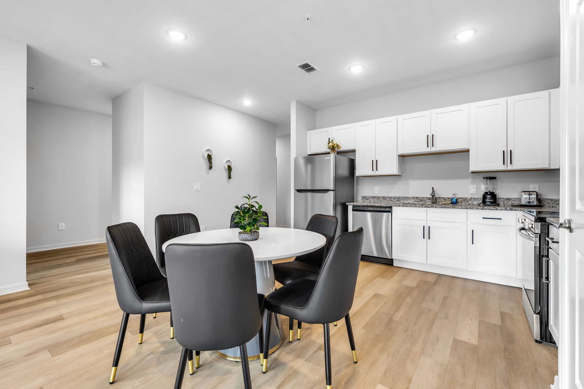 Una cocina moderna con gabinetes blancos, electrodomésticos de acero inoxidable y un comedor con una mesa redonda y sillas negras.