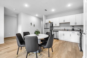 A modern kitchen with white cabinets, stainless steel appliances, and a dining area with a round table and black chairs. - Shire Village (Ocala)
