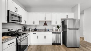 A modern kitchen with white cabinets, stainless steel appliances, and a granite countertop.