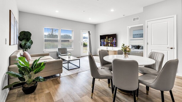 A modern living room with a sofa, coffee table, dining table with chairs, a potted plant, and a television.