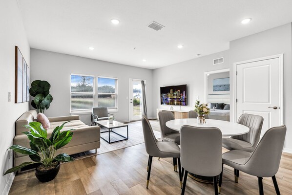 A modern living room with a sofa, coffee table, dining table with chairs, a potted plant, and a television.