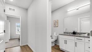 Une salle de bain moderne avec des meubles blancs, un comptoir en granit et un grand miroir.