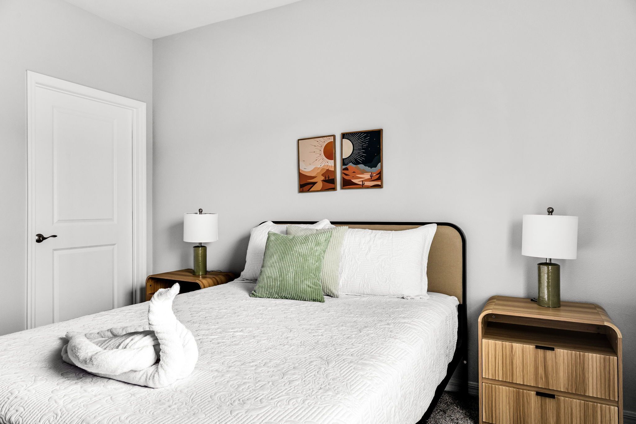 A hotel room with a bed, two bedside tables, a door, and two wall-mounted lamps.