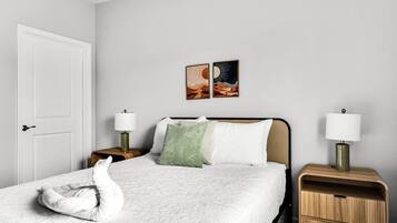 A hotel room with a bed, two bedside tables, a door, and two wall-mounted lamps.