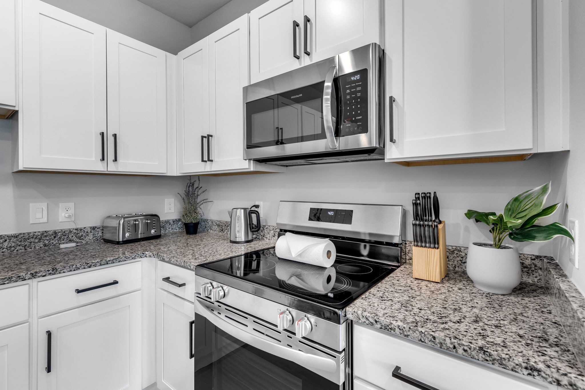 Una cocina moderna con gabinetes blancos, electrodomésticos de acero inoxidable, encimeras de granito y horno empotrado.