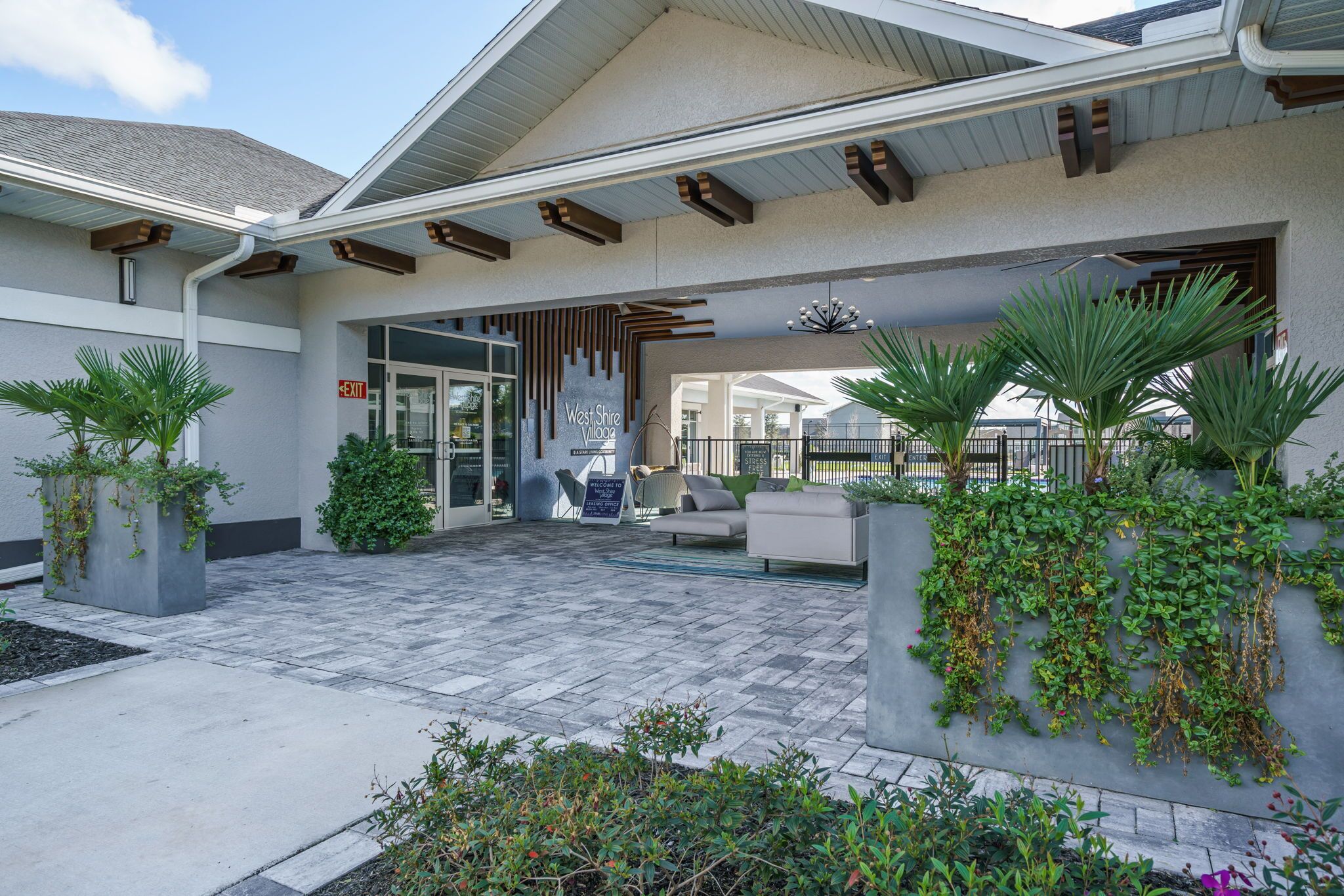 A modern building entrance with a covered patio area, outdoor seating, and potted plants.