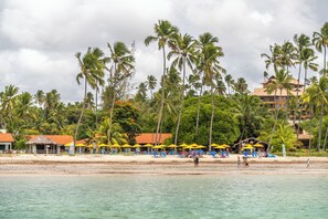 Ein Strand mit Palmen, ein Hotel mit gelben Sonnenschirmen und einem klaren Himmel.