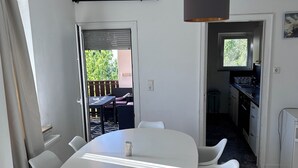 Et moderne spiseområde med et rundt bord og hvide stole, en loftlampe og udsigt til det fri.