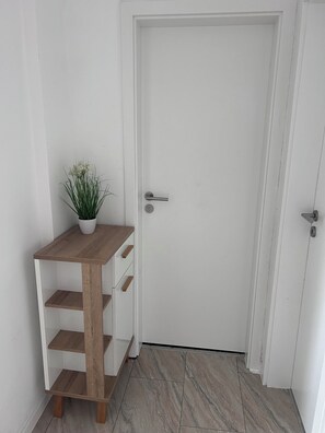 A white door with a silver handle, a small wooden table with a plant on top, and a marble-tiled floor.