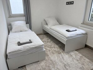 A bedroom with two single beds, a white carpet, and a window with curtains.