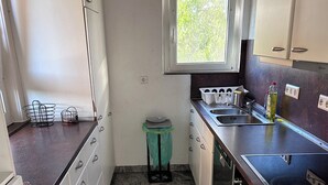 Et kompakt køkken med hvide skabe, en bordplade i granit, et vindue og en lille skraldespand.
