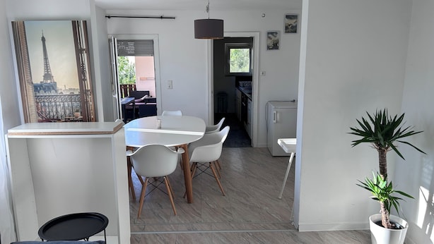 Et moderne køkken med et køleskab, et spiseområde med et hvidt bord og stole, samt en potteplante.
