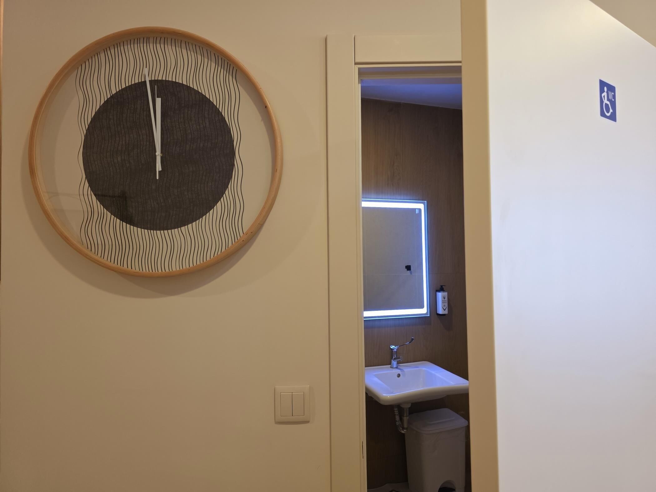 Une salle de bain avec un miroir rond, un lavabo et une poubelle.