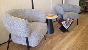Una habitación moderna con dos sillones tapizados grises, una mesita redonda y un atril para revistas.