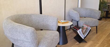 Une pièce moderne avec deux fauteuils gris à revêtement en tissu, une petite table ronde et un présentoir à magazines.