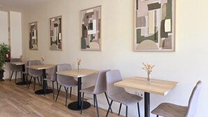 Un comedor con mesas y sillas, arte abstracto en las paredes y una planta en maceta.