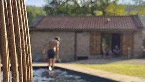 A swimming pool with a person in the water, a building with a tiled roof, and a fence in the foreground. - Casa Rio D'Além | Eco-sustainable | Swimming pool | River | Pure Nature (Parada do Monte e Cubalhão)