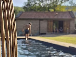 Ein Schwimmbecken mit einer Person darin, ein Gebäude mit einem Ziegeldach und ein Zaun im Vordergrund.