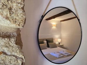 Ein Schlafzimmer mit Bett, Kissen, Nachttisch, Lampe und Spiegel.