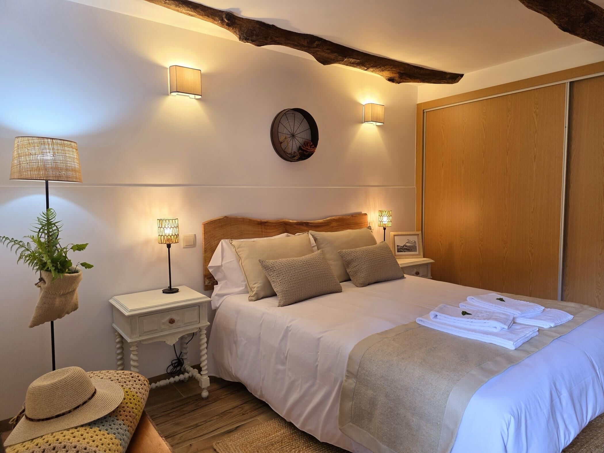Un dormitorio ordenado con cama, lámparas de noche, un reloj de pared y un armario de madera.