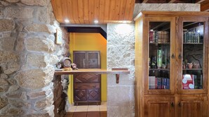 A rustic interior with stone walls, wooden beams, a shelf with a barrel, and a wooden cabinet with glass doors. - Villa Vetusta | Rustic | Pool | Northern Portugal (PENSO)