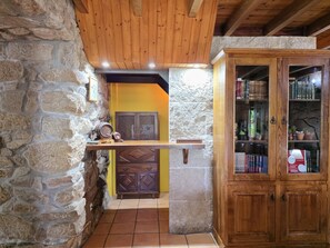 Ein rustikaler Innenraum mit Steinwänden, Holzbalken, einem Regal mit Fass und einem Holzschrank mit Glastüren.